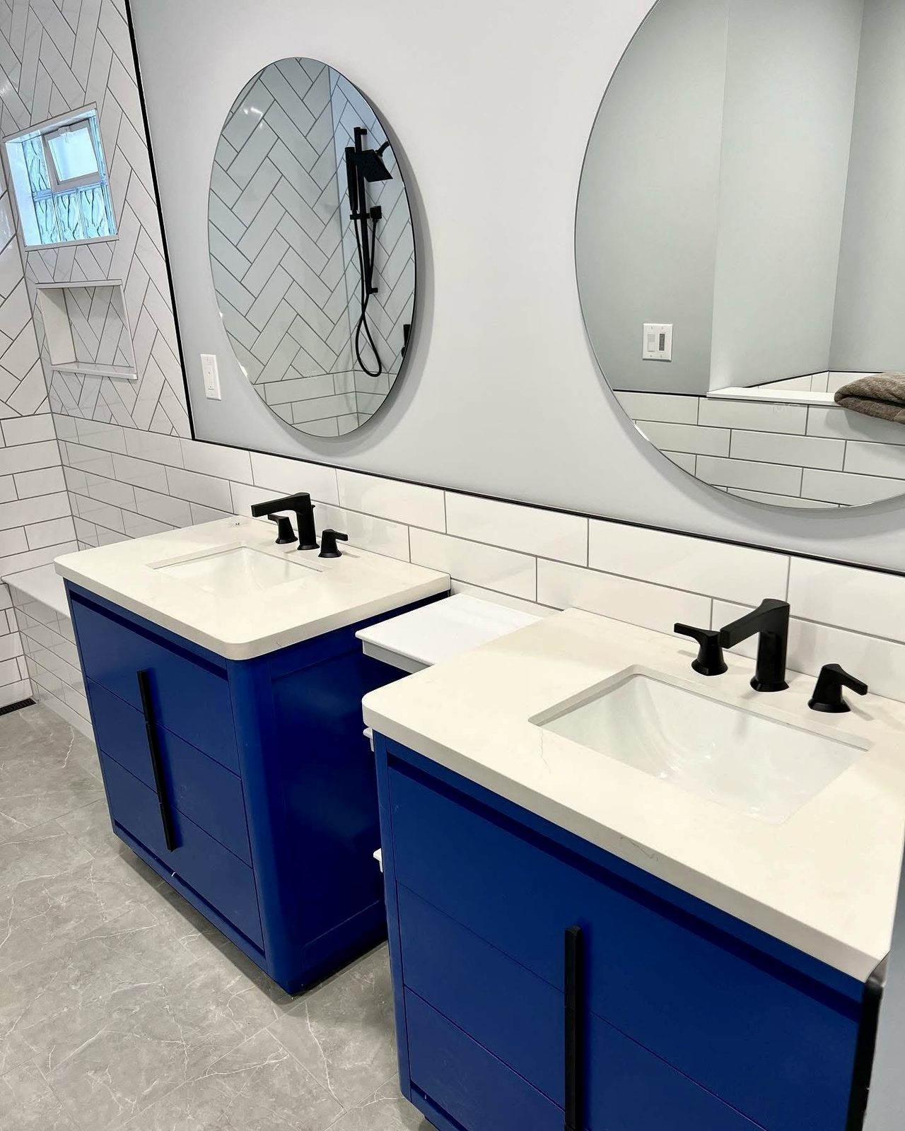Double vanity with cobalt blue cabinets, a quartz top, undermount sinks and round mirrors against white subway tile