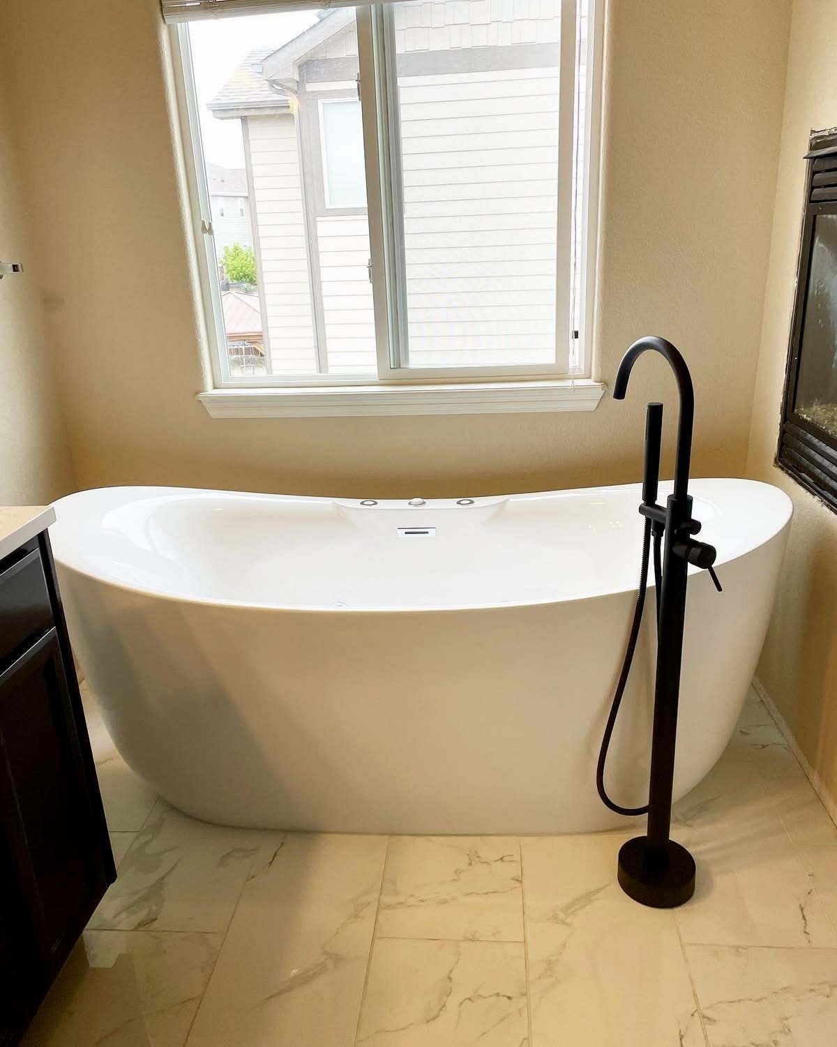 Freestanding soaking tub with a black floor-mounted tub filler and handshower