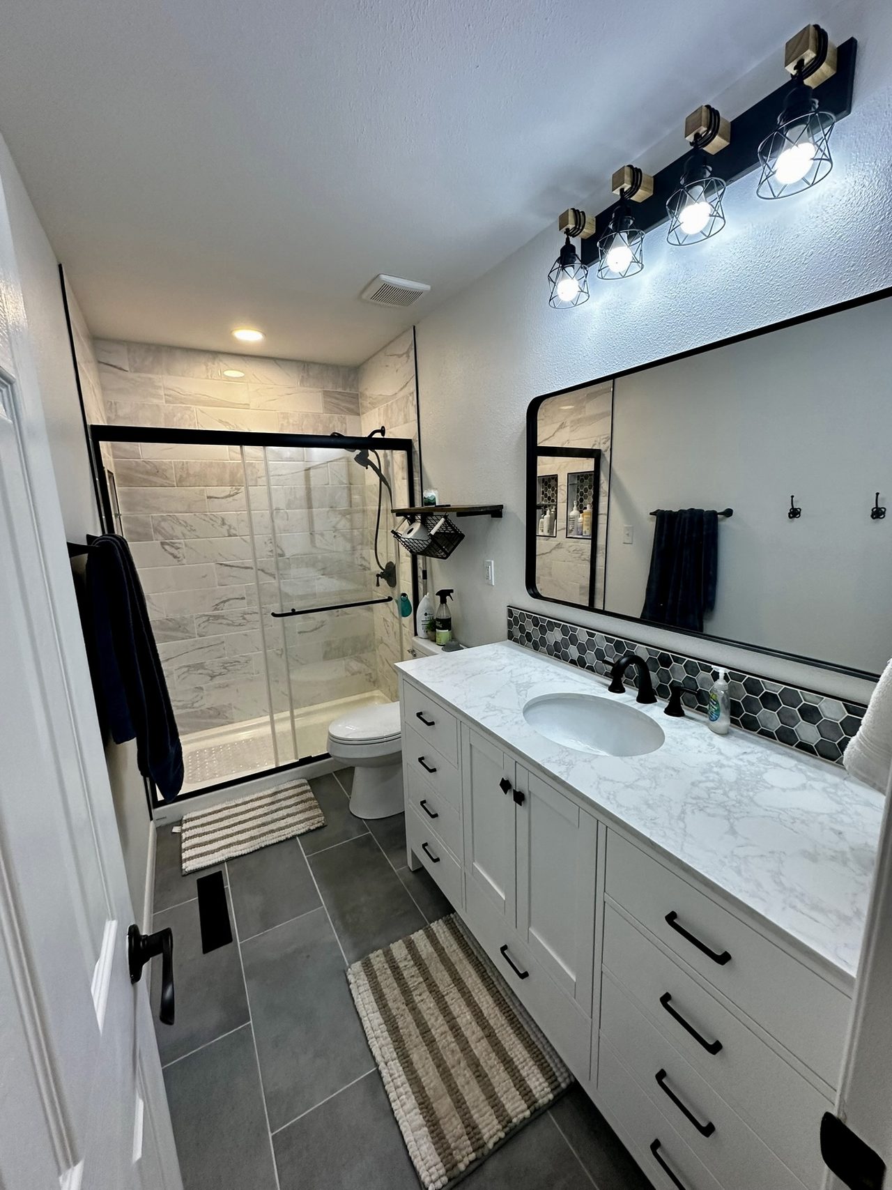 Finished bathroom with a glass shower enclosure, marble-look tile, a white vanity and black fixtures