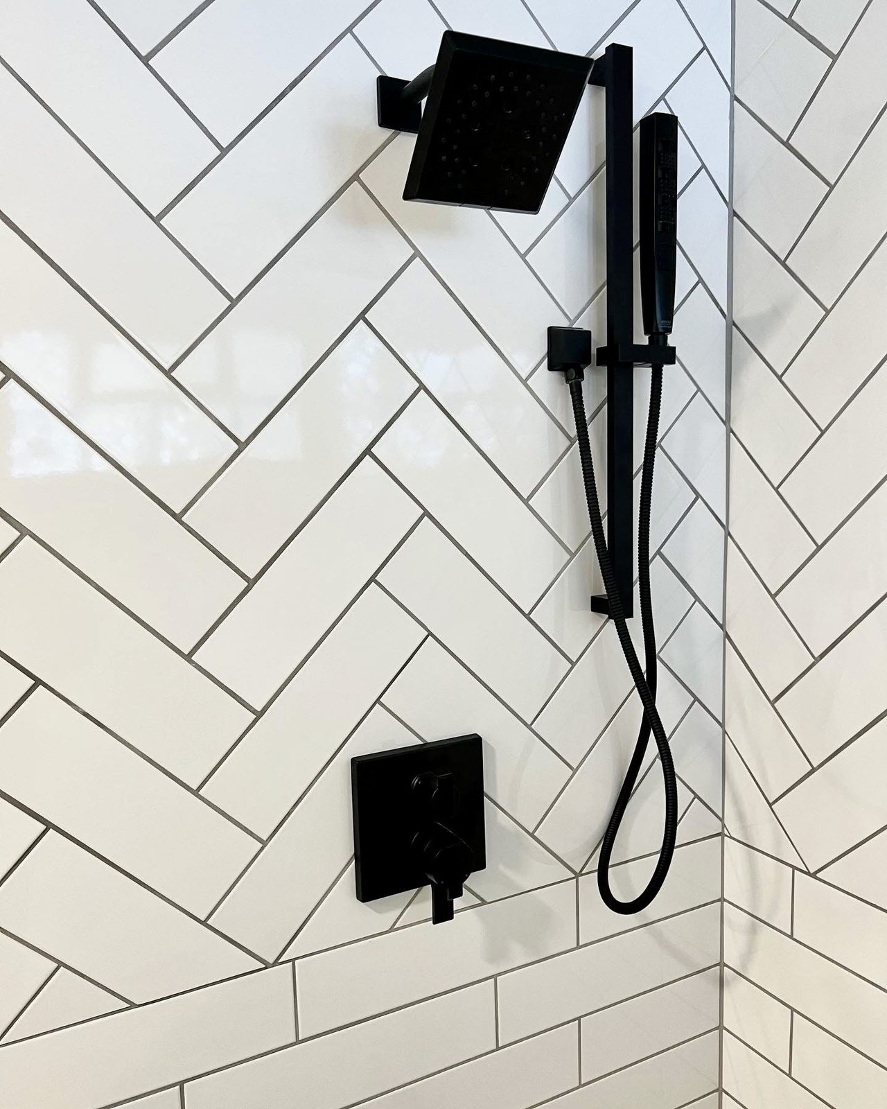 White herringbone tile shower wall with a black shower valve and slide bar