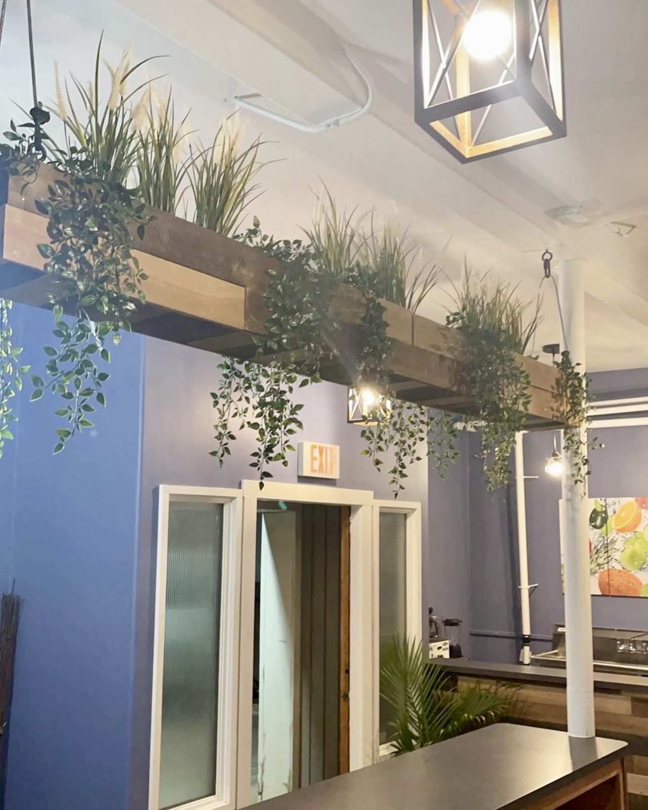 Timber pergola with trailing greenery over a café floor, pendant lighting and exposed conduit above