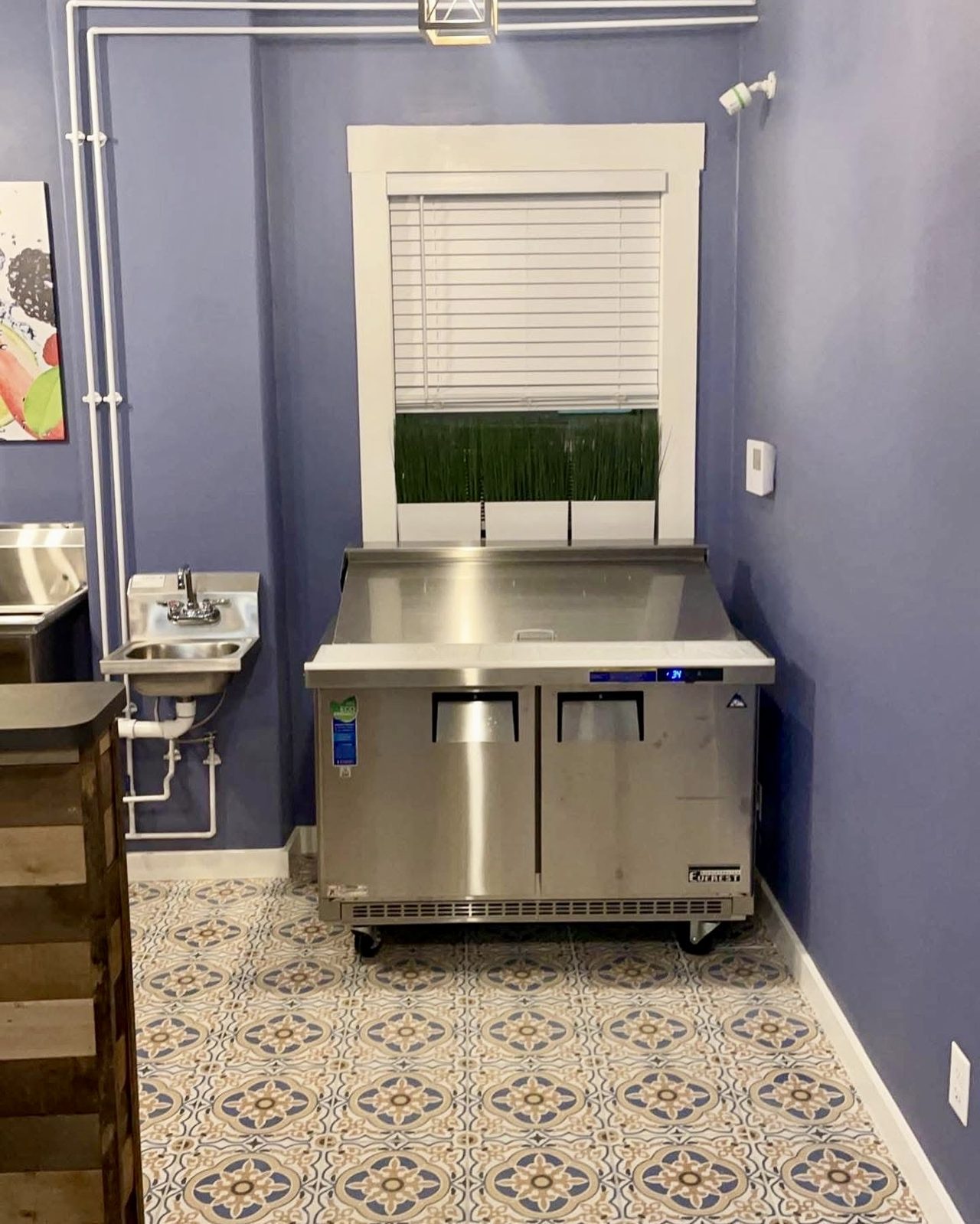 Commercial kitchen with a refrigerated prep table and a wall-mounted hand sink on tiled floor