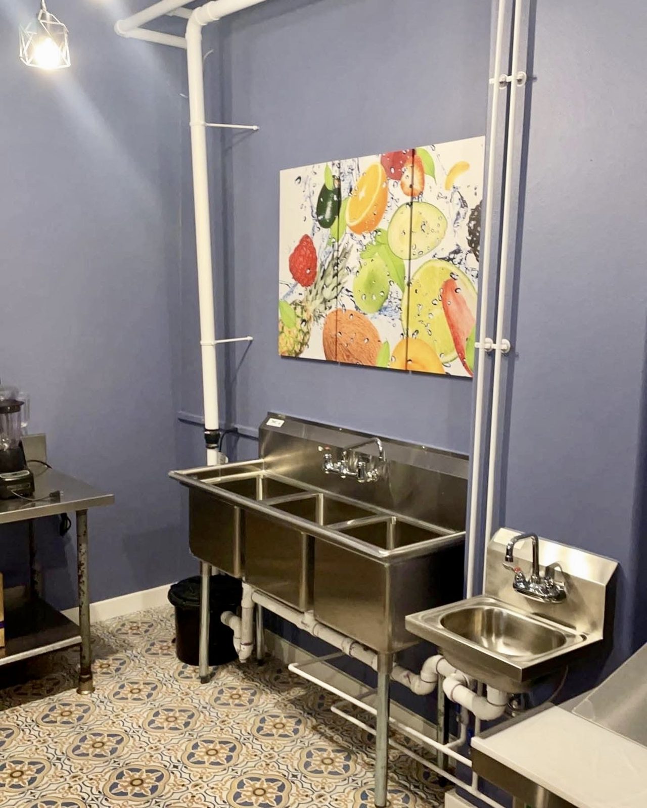 Three-compartment stainless sink with a separate hand sink and exposed conduit in a commercial kitchen