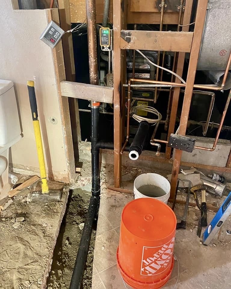 Under-slab waste line and copper supply roughed in through a trenched concrete floor, wall left open for inspection