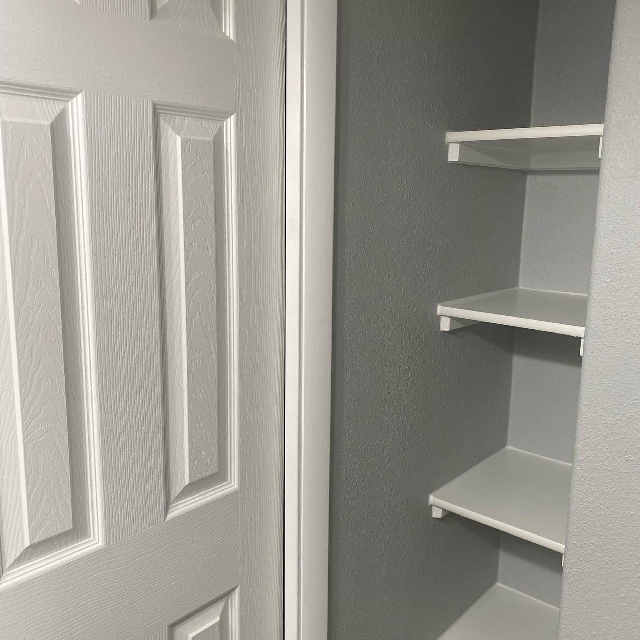 Painted wall with white floating shelves beside a white panel door