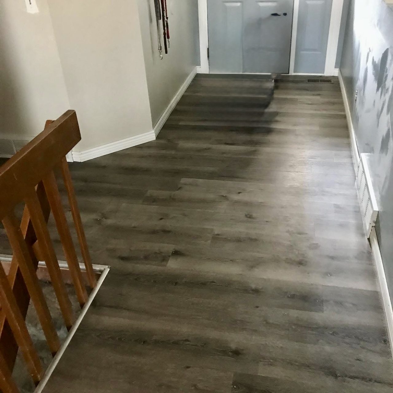 Gray luxury vinyl plank flooring running through a hallway to a stair newel post