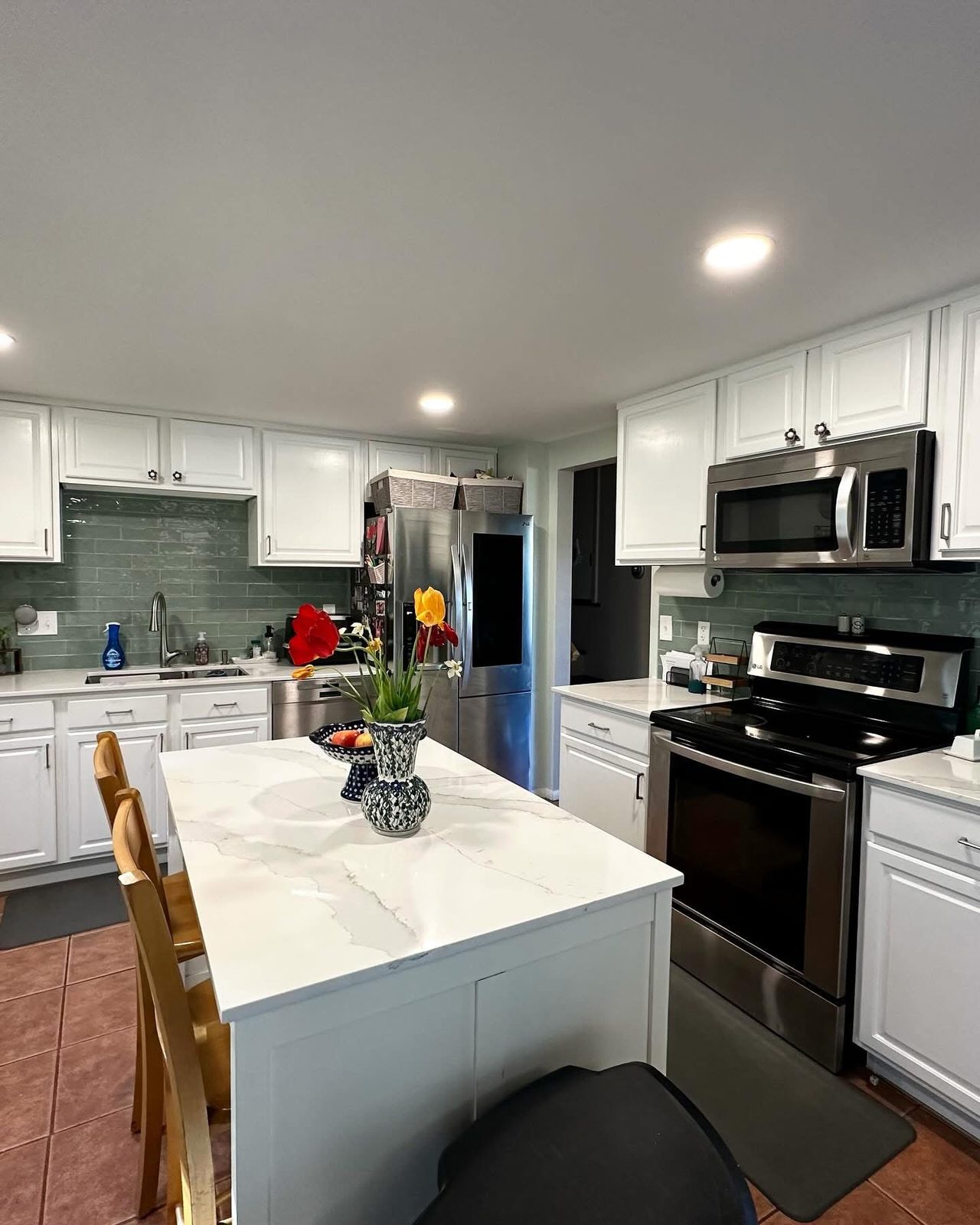 Kitchen with white cabinets, green glass subway tile backsplash and a quartz waterfall island